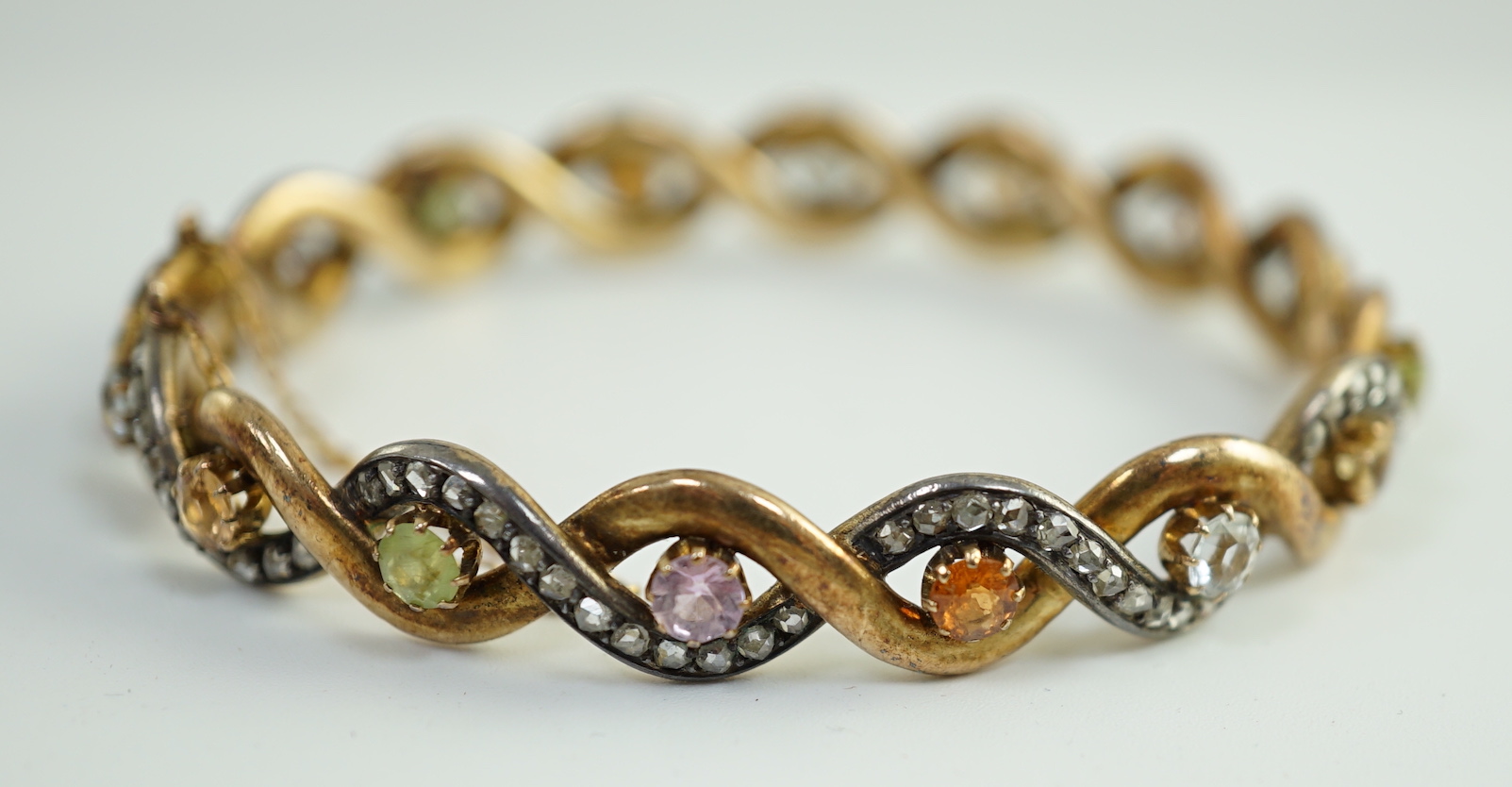 A late 19th/early 20th century French 18ct gold and silver rose cut diamond and multi gem set spiral hinged bangle